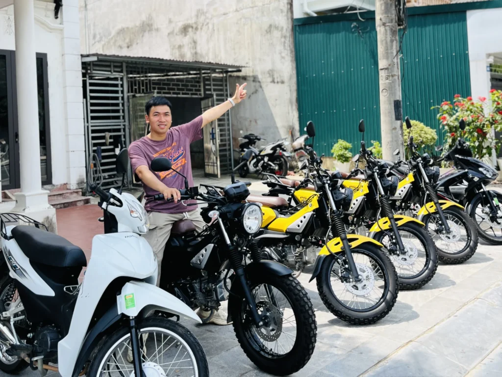 Ha Giang motorbike rental – owner sitting on a motorbike in front of rental shop with available bikes for Ha Giang Loop