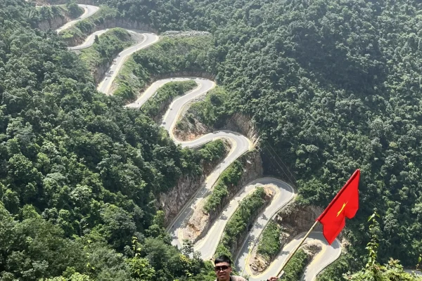 ảnh một anh hướng dẫn viên trên viewpoint đèo khau cốc trà, cầm một cây cờ việt nam trên tay với background là đèo khau cốc trà tại cao bằng